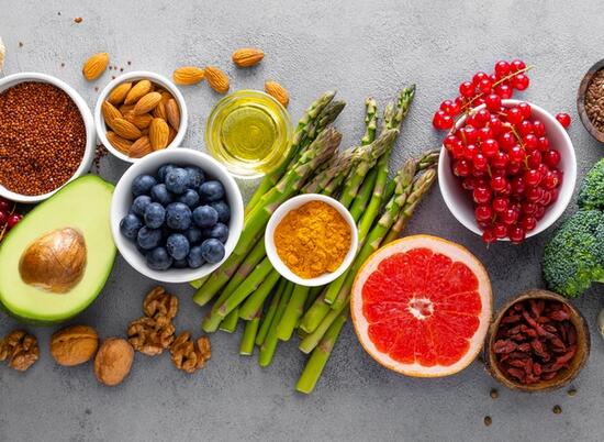 A potpourri of vegetables, fruits ad seasoning spread out across a marble surface.
